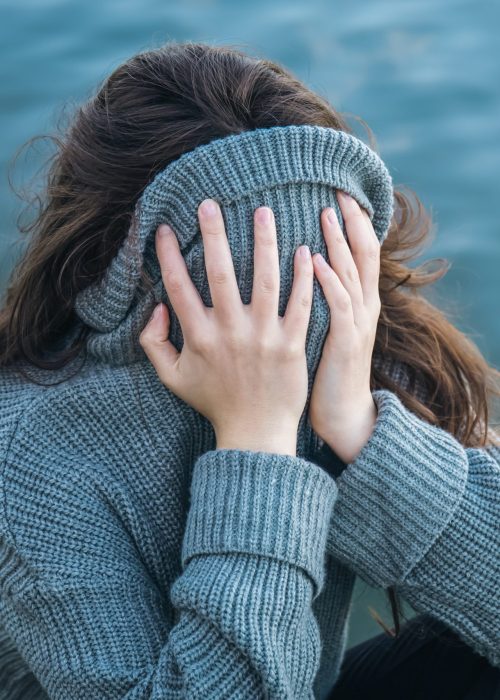 A woman hid her face in a sweater while sitting by the sea, the concept of mental health and mood.
